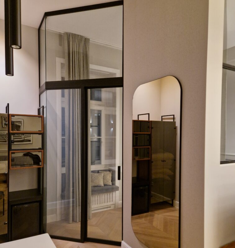 Interior view of a showroom featuring large mirrored glass doors and dark wood frames, with beige walls and light wood flooring.